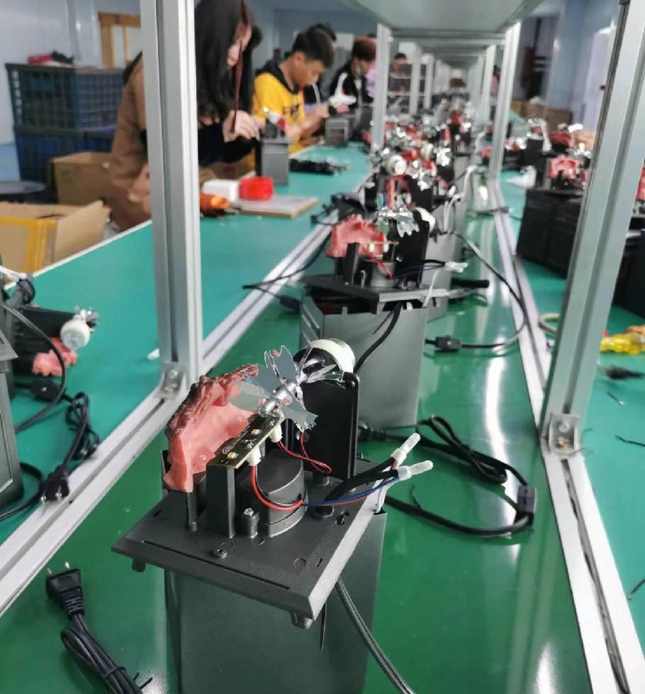 An assembly line for animated figures: motor and gearbox units on stamped steel bases, wiring harnesses and moulded power cords, with painted heads being fitted