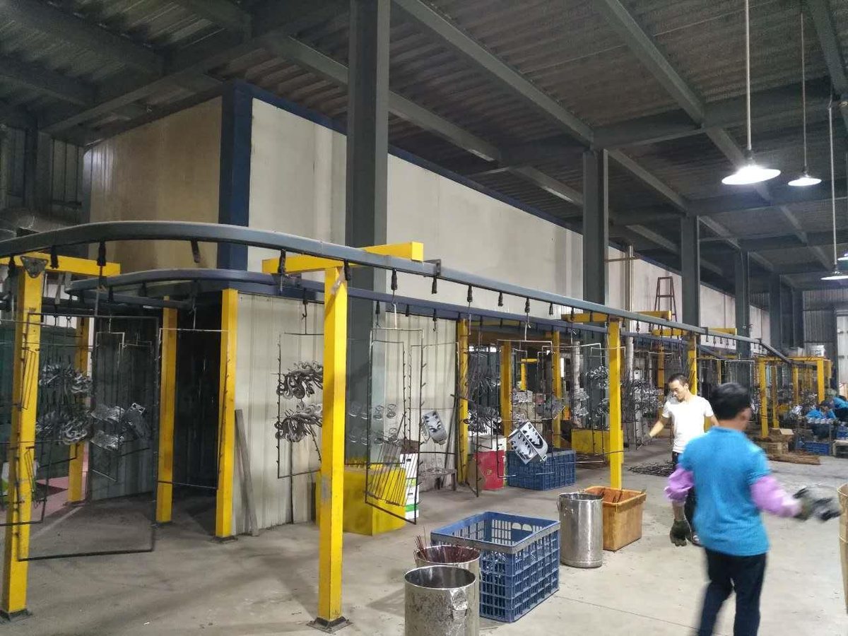A powder coating line: racked metal parts hanging from an overhead conveyor feeding into the coating booth