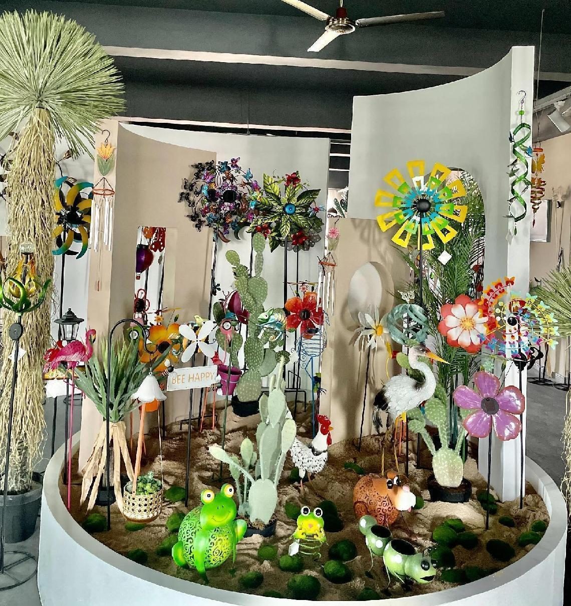 A garden display island: painted metal flowers, spinners, birdhouses and gnomes arranged around a planted bed