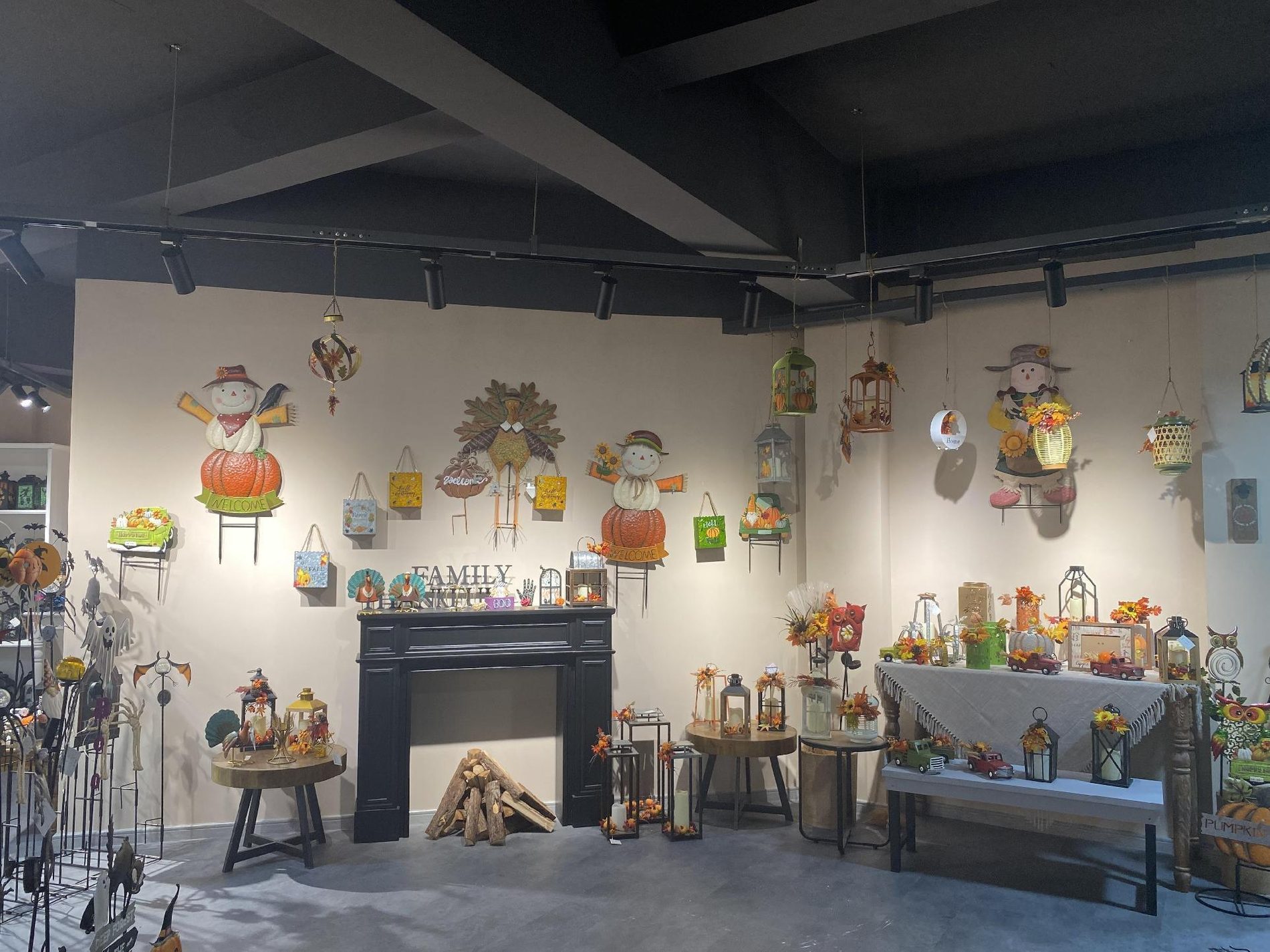 An autumn room set in the showroom: scarecrow and pumpkin wall pieces above a black fireplace, with lanterns and harvest pieces on side tables